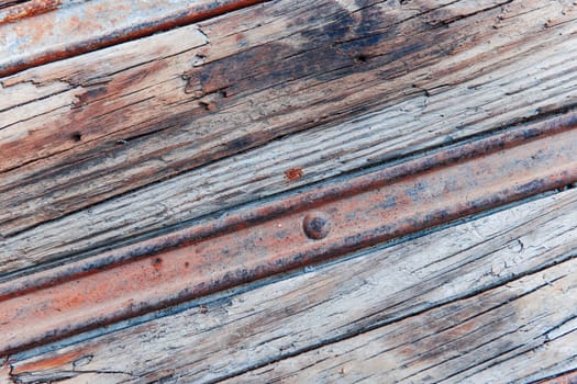 Format-filling view of a rusty metal rail in the weathered wood in an oblique view.