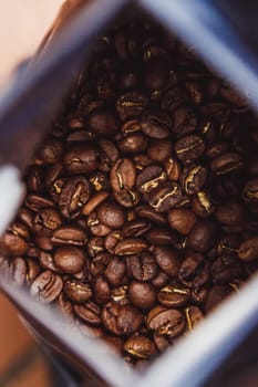 Coffee beans in a plastic foil package on wooden background. Roasted aromatic coffee top view