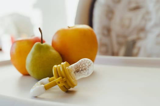 Nibbler with fresh apples and pear on light kids table, closeup. Baby feeder.