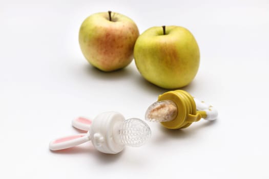 Nibbler with fresh apples on white table, closeup. Baby feeder.