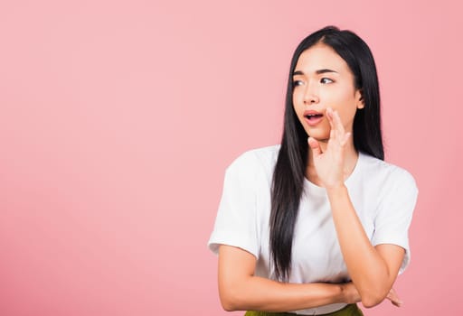 Asian happy portrait beautiful cute young woman teen standing hand on mouth talking whisper secret rumor studio shot isolated on pink background, Thai female looking to side away with copy space