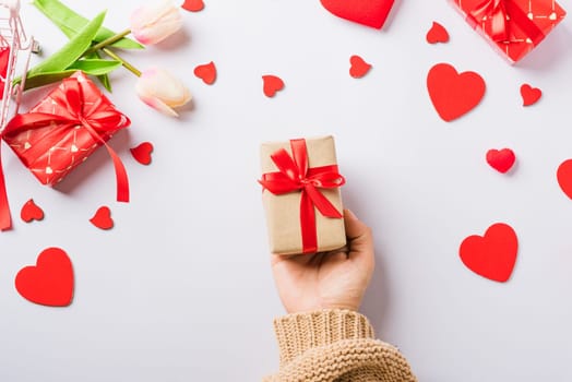 Valentine's day and birthday. Woman hands holding gift or present box decorated and red heart surprise on white background, Female's hand hold gift box package in craft paper Top view flat lay