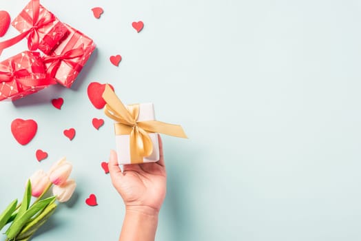 Valentine's day and birthday. Woman hands holding gift or present box decorated and red heart surprise on blue background, Female's hand hold gift box package in craft paper Top view flat lay