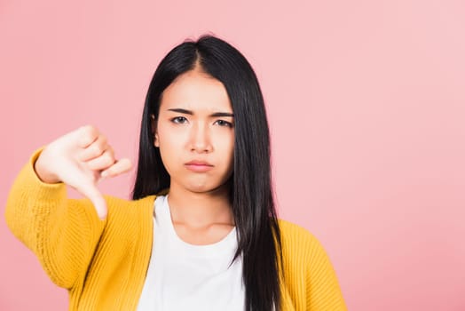 Portrait Asian beautiful young woman unhappy, negative gesture showing finger thumbs down or dislike sign, studio shot isolated on pink background, Thai female rejection unlike with copy space