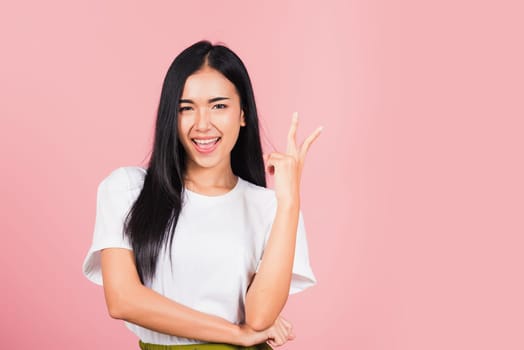 Asian happy portrait beautiful cute young woman teen smile standing show finger making v-sign victory sign gesture side away looking to camera studio shot isolated on pink background with copy space