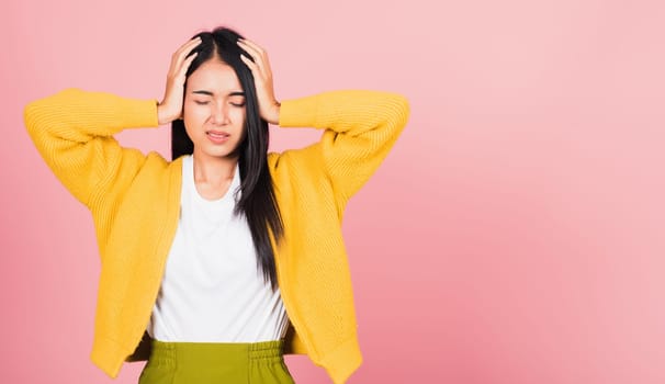 Portrait of beautiful Asian young woman sad tired strain face holding hold head by hands, female person closed eyes problem she headache, studio shot isolated on pink background
