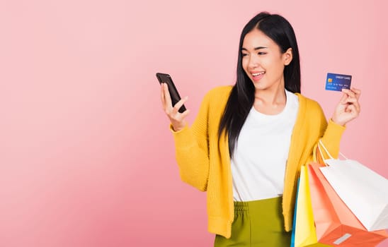 Portrait Asian happy beautiful young woman shopper smiling standing excited holding online shopping bags colorful and credit card for payment on hand in summer, studio shot isolated on pink background