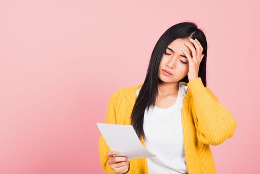 Portrait of beautiful Asian young woman sad tired strain holding paper calculating bills on hand, female person problem she hold worried over bill, studio shot isolated on pink background