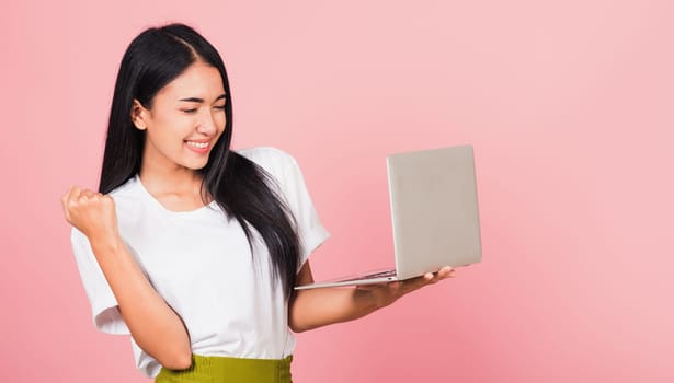 Portrait of happy Asian beautiful young woman teen confident smiling face holding using laptop computer and excited celebrating success, studio shot isolated on pink background, with copy space