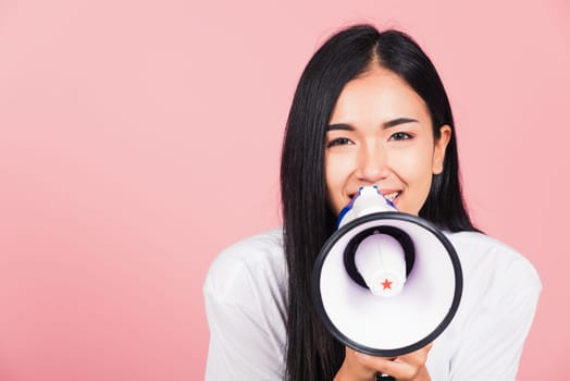 Portrait of happy Asian beautiful young woman teen confident smiling face holding making announcement message shouting screaming in megaphone, studio shot isolated on pink background, with copy space