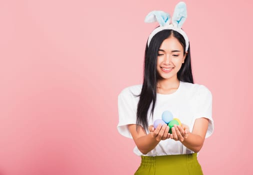Happy Easter concept. Beautiful young woman smiling wearing rabbit ears holding colorful Easter eggs gift on hands, Portrait female looking at eggs, studio shot isolated on pink background