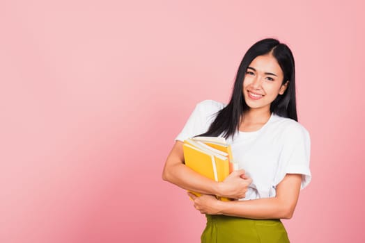 Portrait of beautiful Asian young woman teenage smiling hugging books, female person holding book multicolor, studio shot isolated on pink background with copy space, education concept