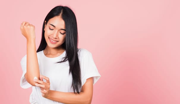 Portrait of Asian beautiful young woman applying lotion cosmetic moisturizer cream on her elbow skin, studio shot isolated on pink background, Healthcare medical and hygiene skin body care concept