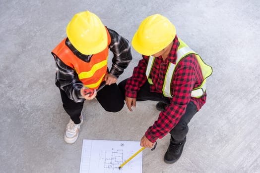 Architect and client discuss help create plan with blueprint of the building at construction site floor. Asian engineer foreman worker man and woman meeting talking on drawing paper project, top view