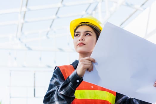 Asian engineer architect worker woman holding blueprint infrastructure progress at construction site, engineering female leader standing hold paper plan control worker to building project