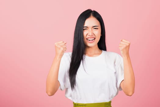 Asian happy portrait beautiful cute young woman standing angry and mad raising fist frustrated and furious while shouting with anger isolated, studio shot on pink background and copy space