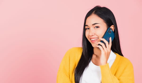Portrait Asian happy beautiful young woman smile talking by smartphone looking to camera isolated, studio shot isolated on pink background, Thai female hold the phone to calling with copy space