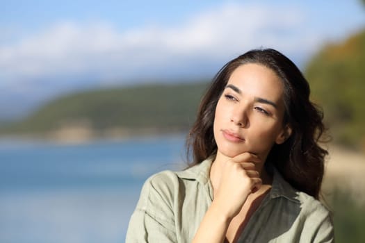 Pensive woman thinking looking at side in a lake