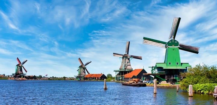 ZAANSE SCHANS, NETHERLANDS - CIRCA AUGUST 2020: Dutch windmill in green countryside close to Amsterdam, with blue sky and river water.