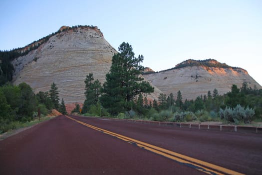 The red paved road towards the white Checkerboard Mesa during a summer sunset in Zion National Park in Utah