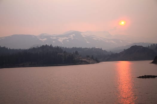 The sun reflecting on the lake through the fog and the ash of a wildfire in Yosemite National Park in California