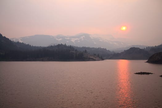 The sun reflecting on the lake through the fog and the ash of a wildfire in Yosemite National Park in California