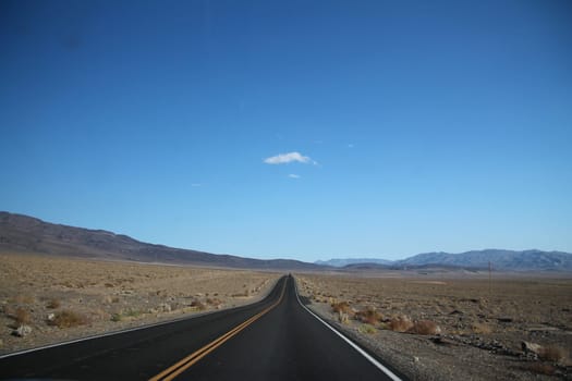 Straight road towards mountain range in horizon at Death Valley in California
