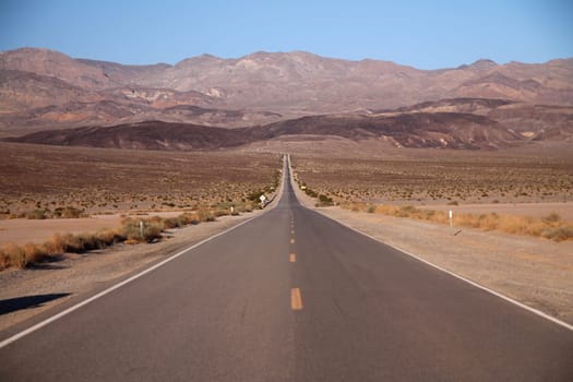 Looking down the middle of a long straight desert road with no one in site for miles in the Death Valley in California