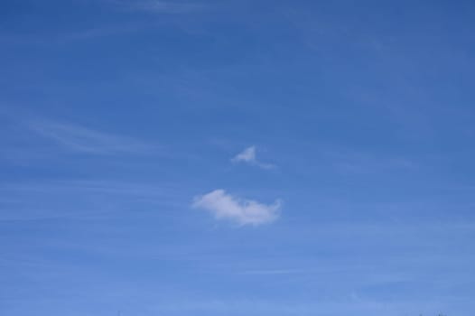 Soft clouds float effortlessly against a clear blue sky on a tranquil afternoon, creating a peaceful ambiance.