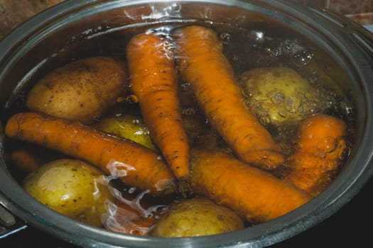 Potatoes and carrots boiling in a pot with hot water. preparing vegetables for salad