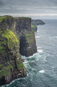 Tourists walking on Cliffs of Moher with watchtower Moher Tower on far distance, popular tourist attraction, Wild Atlantic Way, County Clare, Ireland