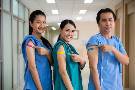 Medical personnel pointing to bandage with plaster on arm after getting against Covid-19 vaccine, happy nurse woman and man standing at hospital, Covid-19 vaccination concept