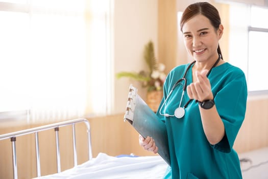 Portrait of a smiling nurse or medical staff make a mini heart hand sign in a hospital, happy woman doctor in uniform holding clipboard, people medical healthcare concept
