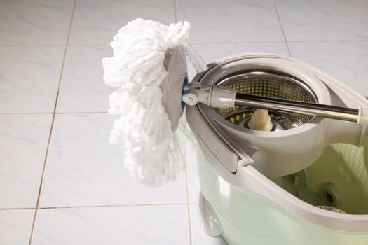 Mop with microfiber head spinning on the bucket next to floor cleaning liquid and mopping the floor house in the living room