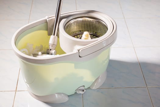 Mop with microfiber head spinning on the bucket next to floor cleaning liquid and mopping the floor house in the living room