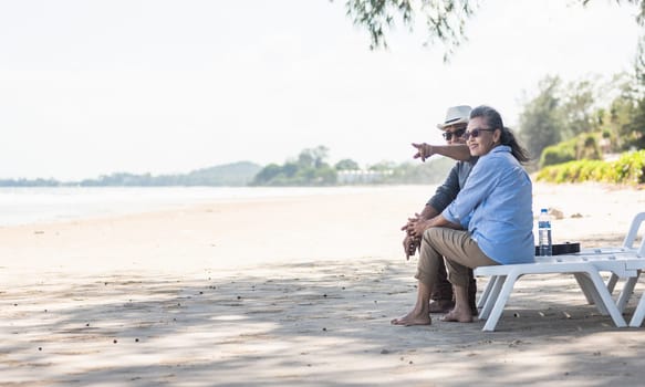 Happy Asian family, senior couple sitting on chairs with backs on beach travel vacation talking together, Romantic elderly enjoy Travel summer vacation, plan life insurance retirement couple concept