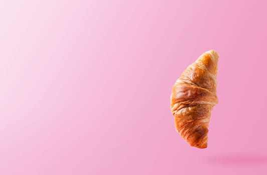 Freshly baked croissant levitating or flying. Croissant fly in the air isolated on pink background. Levitation scene. Copy space place. Signboard mockup or advertisement of bakery, confectionery