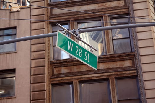 Green big West 28th Street sign hanging on a arch pole in the streets of midtown Manhattan in New York City