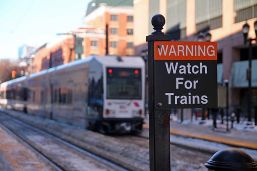 Warning Watch for Trains black and red sign with a streetcar on the back in a sunny day with snow on the ground