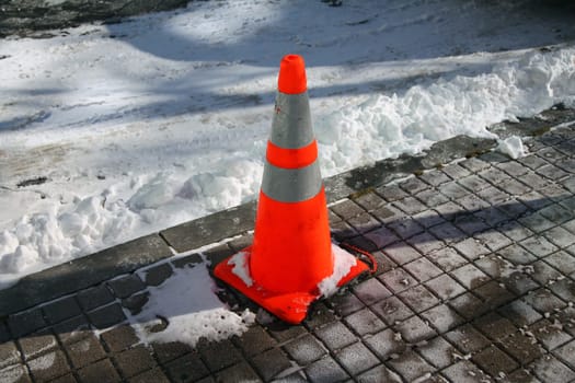 An orange street cone in the snow on a sunny winter day