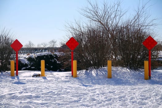 Red end of the road square sign with three yellow poles on the snow in a sunny day after a storm