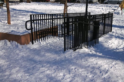 A black fence on the white snow in a park during a sunny winter day