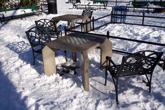 A concrete chessboard table with a heavy iron chair in the snow in the park