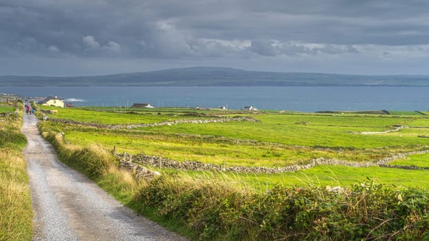 Tourists walking down the country road from popular attraction, iconic Cliffs of Moher, Wild Atlantic Way, County Clare, UNESCO, Ireland