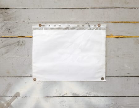 White paper sign with rivets, vintage background on a gray wooden old backdrop. Wooden textured wall, weighs a white blank cardboard sign lit by the sun, closeup.