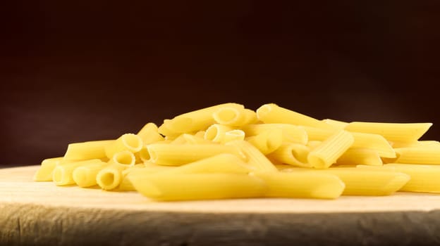 Penne Rigate Raw Pasta is a short pasta with oblique cuts and a ribbed surface. Traditional Italian pasta. Pasta background. Side view of an Italian food ingredient on a wooden plate