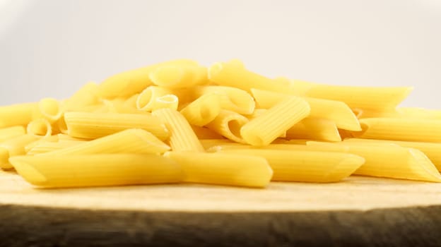 Penne Rigate Raw Pasta is a short pasta with oblique cuts and a ribbed surface. Traditional Italian pasta. Pasta background. Side view of an Italian food ingredient on a wooden plate