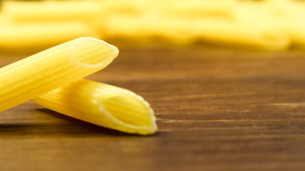 Penne Rigate Raw Pasta is a short pasta with oblique cuts and a ribbed surface. Traditional Italian pasta. Pasta background. Side view of Italian food ingredient on brown table. Copy space.