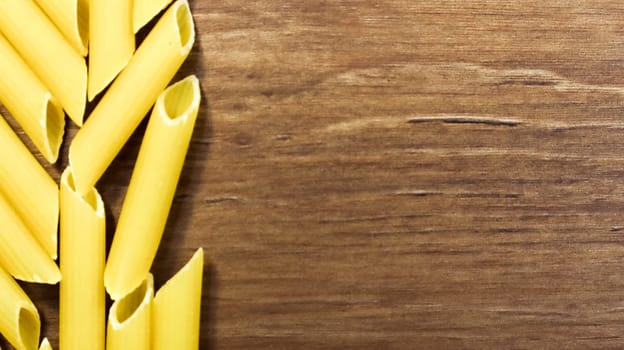 Penne Rigate Raw Pasta is a short pasta with oblique cuts and a ribbed surface. Traditional Italian pasta. Pasta background. Top view of Italian food ingredient on brown table. Copy space.