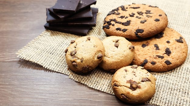 American chocolate chip cookies on a brown wooden table and on a linen napkin close-up. Traditional rounded crunchy dough with chocolate chips. Bakery. Delicious dessert, pastries. Rural still life